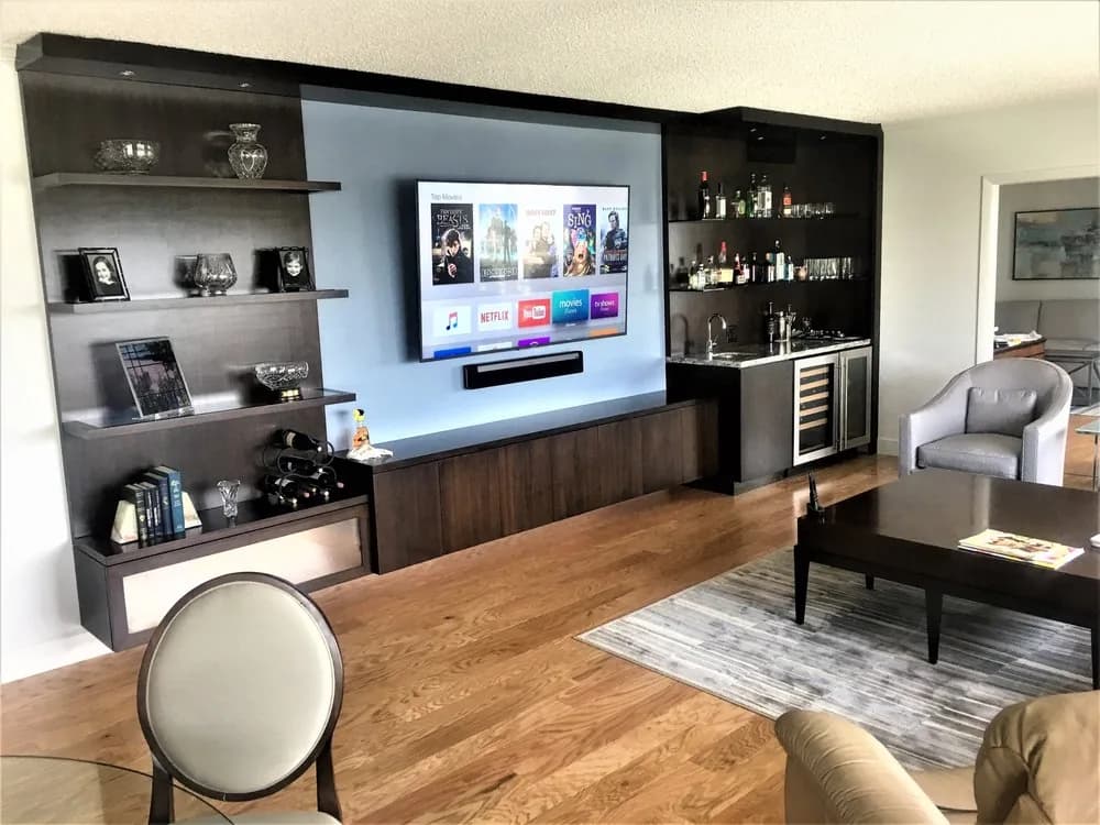 Dark wood media wall with a wall-mounted display and soundbar beside a wet bar