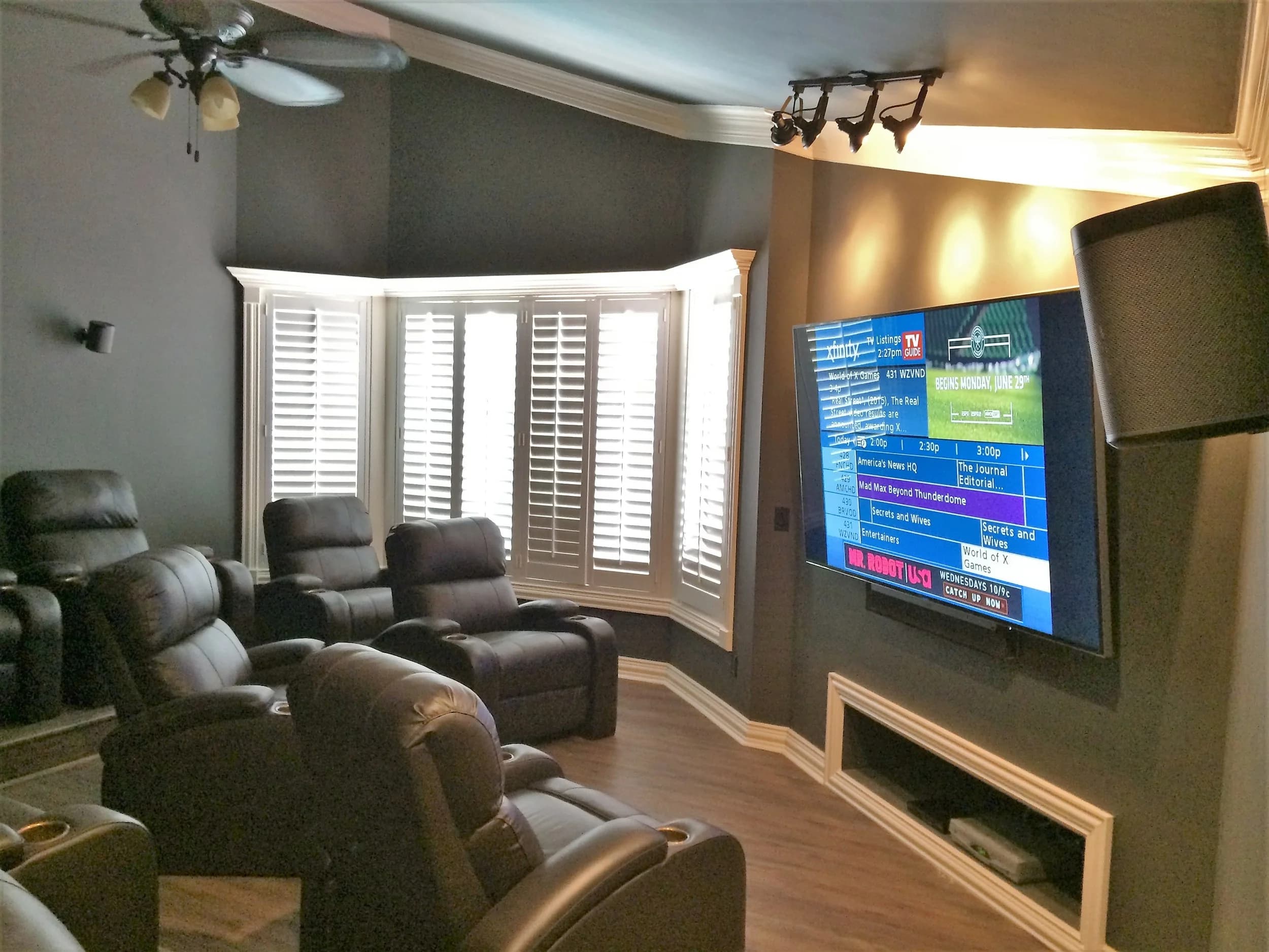 Home theater seating facing a large display, plantation shutters behind