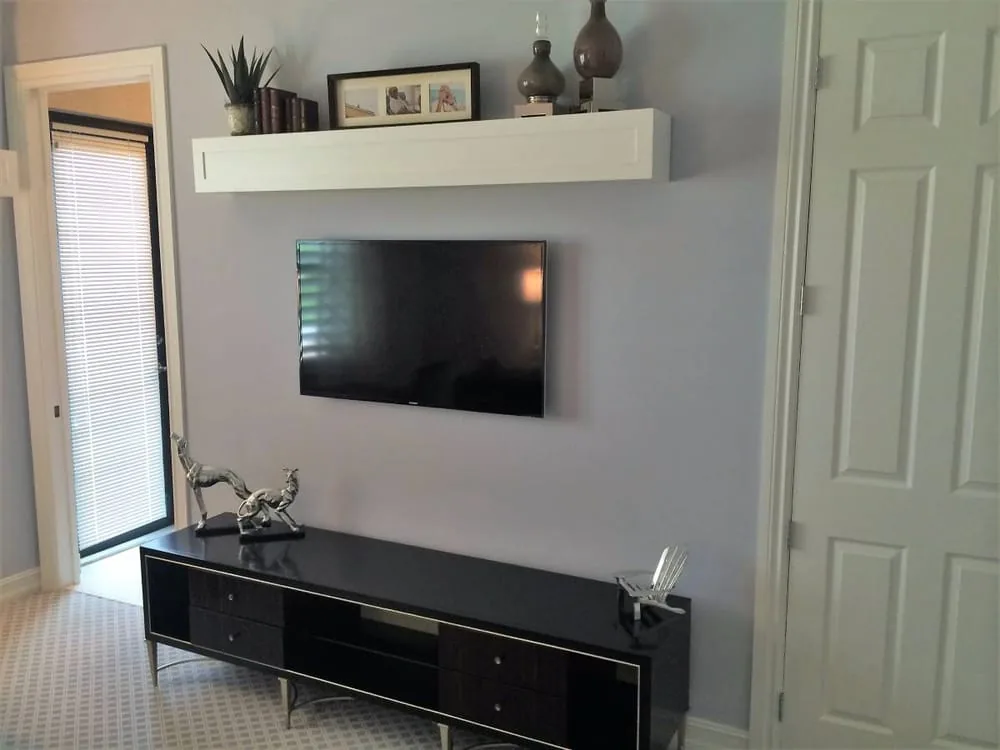 Wall-mounted display under a floating shelf above a low console, no cable on the wall